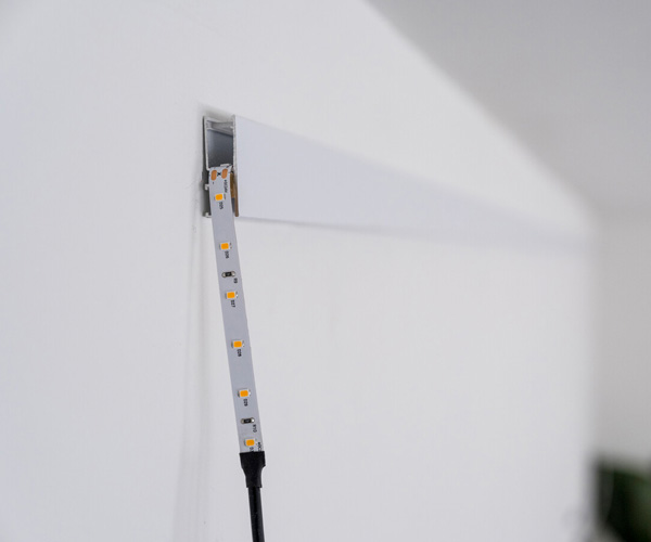 Vertical LED strip light mounted in a metal channel on a white wall, connected to a black power cable.