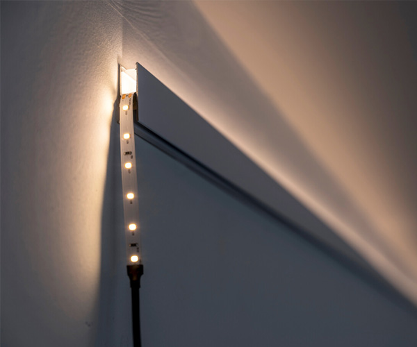 Close-up of a warm-white LED light strip mounted along the edge of a white door frame, casting light on the wall nearby.