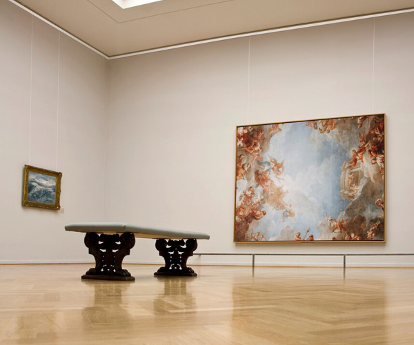 Museum gallery with a long bench and two framed paintings on pale walls, including a large sky-and-leaves work.