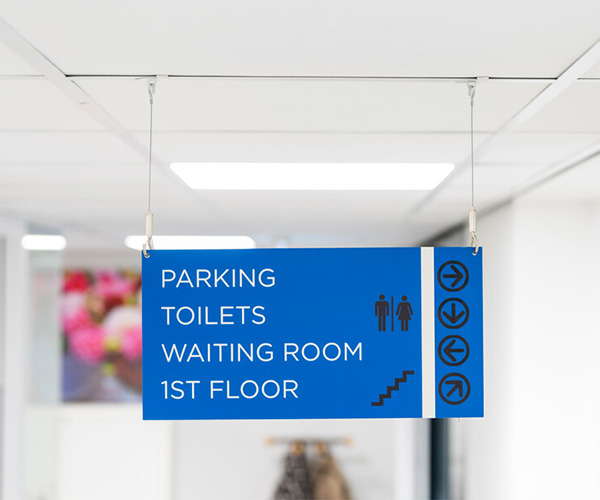 Blue hanging sign listing Parking, Toilets, Waiting Room on the 1st Floor with direction arrows and a staircase icon.